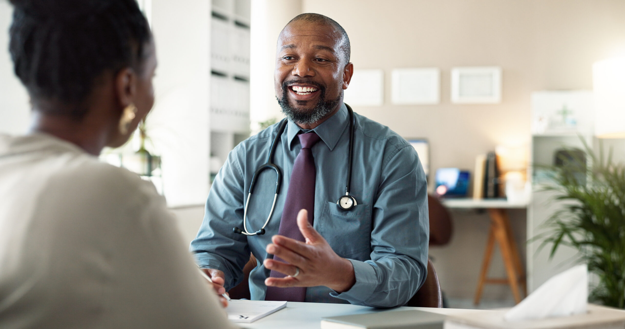 Conversation, healthcare and smile of doctor with patient in office at hospital for consulting or discussion. Feedback, happy and medical professional black man with person in clinic for checkup