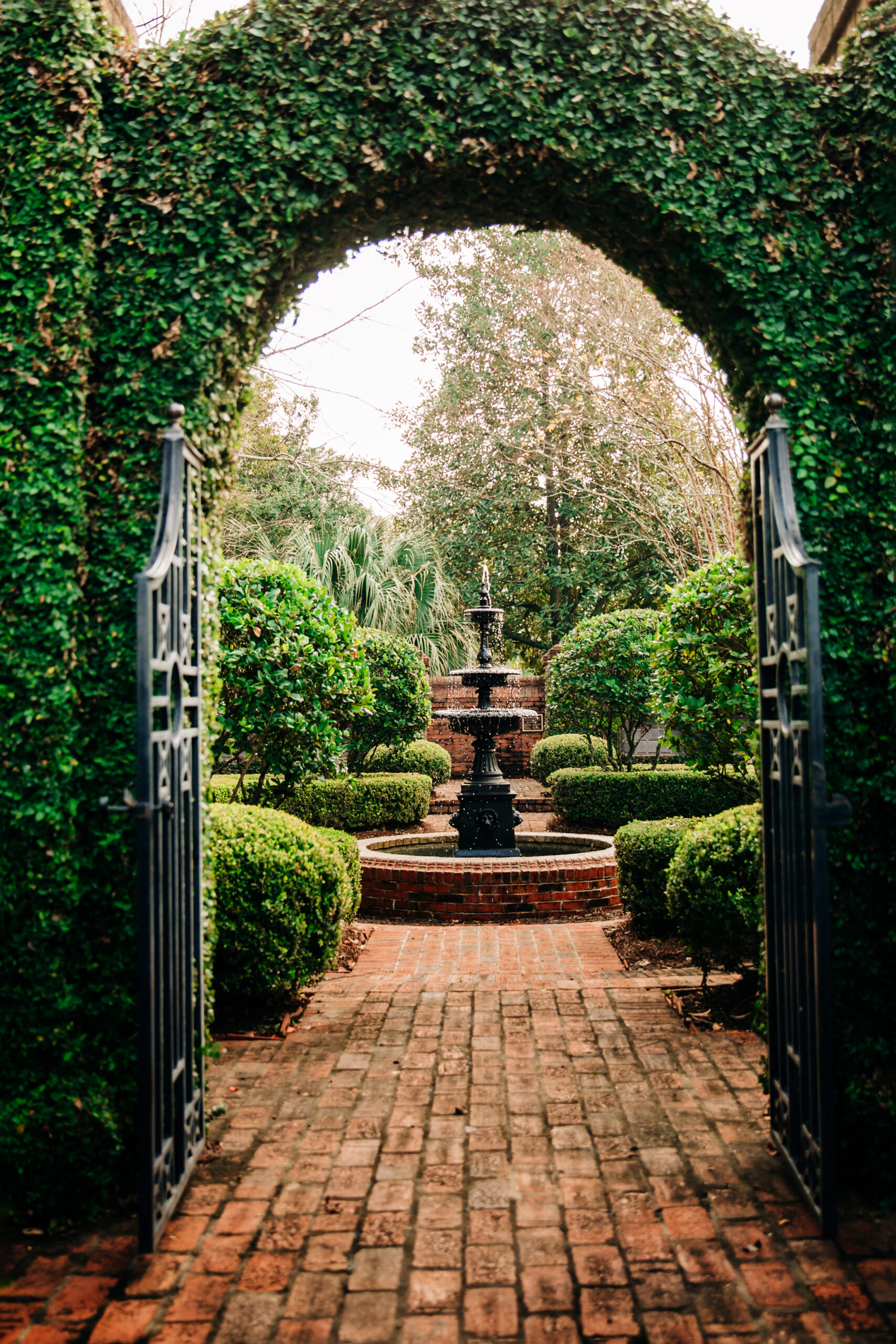 Outdoor Green secret garden with arched entry and gate and a fountain in the middle and red brick and black iron gate